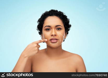beauty, plastic surgery and people concept - young african american woman with arrows on face over blue background. young african american woman with arrows on face