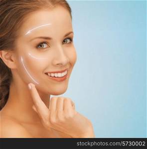 beauty, plastic surgery, anti-aging, people and health concept - beautiful young woman applying creme to her face with lifting arrows over blue background