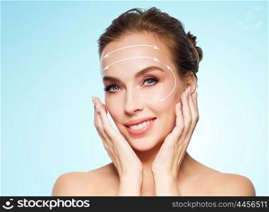 beauty, plastic surgery, facelift, people and rejuvenation concept - beautiful young woman touching her face with lifting arrows over blue background