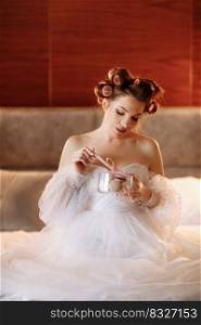 Beauty portrait of a beautiful smiling young brunette woman with bright pin-up make-up eating delicious french macaroons or macarons. girl in white dress and pink curlers sitting on the bed and relax.. Beauty portrait of a beautiful smiling young brunette woman with bright pin-up make-up eating delicious french macaroons or macarons. girl in white dress and pink curlers sitting on the bed and relax