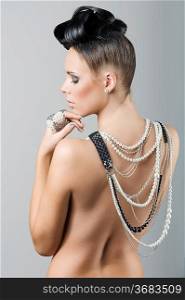 beauty portrait of a naked brunette with creative hair style and covering her back with jewellery