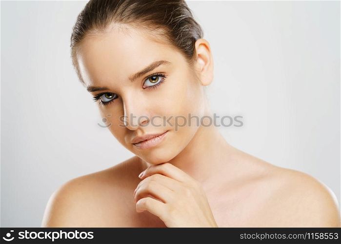 Beauty portrait of beautiful caucasian girl young brunette woman with natural perfect skin and makeup holding hand on chin looking to the camera tied hair