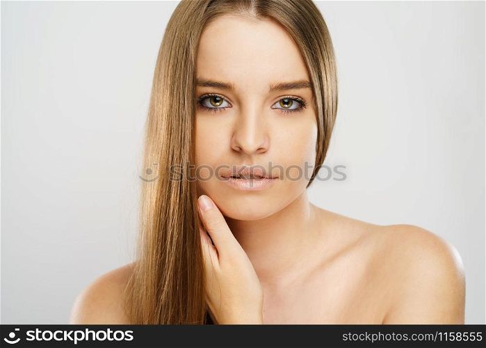 Beauty portrait of beautiful caucasian girl young brunette woman with natural perfect skin and makeup holding hand on neck looking to the camera at studio in front of white background