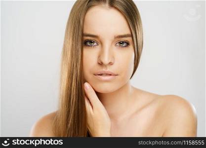 Beauty portrait of beautiful caucasian girl young brunette woman with natural perfect skin and makeup holding hand on neck looking to the camera at studio in front of white background