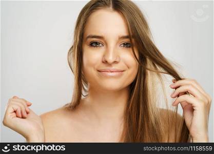 Beauty portrait of beautiful caucasian girl young brunette woman with natural perfect skin and makeup holding hand in hair looking to the camera at studio in front of white background