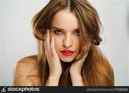 Beauty portrait of beautiful caucasian girl young brunette woman with red lipstick natural perfect skin and makeup holding hands on her chin looking to the camera in studio