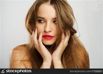 Beauty portrait of beautiful caucasian girl young brunette woman with red lipstick natural perfect skin and makeup holding hands on her chin looking to the side in studio