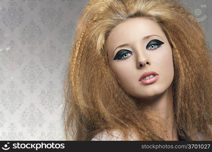 beauty portrait of blonde girl with dark glossy make-up and voluminous rock hair-style on gray background