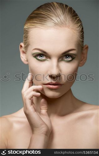 beauty portrait of sensual blonde girl with pretty green make-up and perfect visage skin. Posing with hand near the face