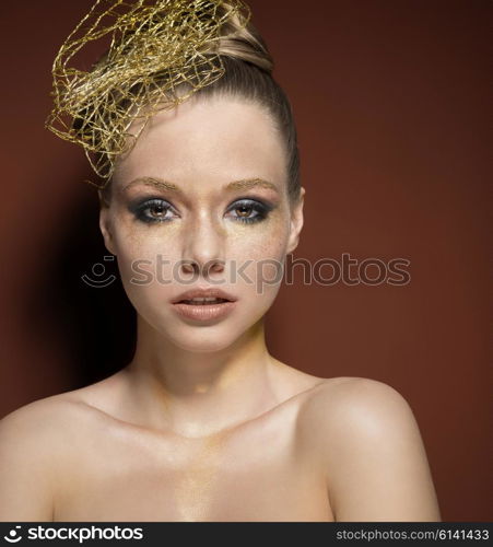 beauty portrait of stunning girl with creative golden glitter make-up, accessory in the hair-style. She is covering her naked breast and looking in camera