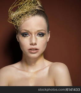 beauty portrait of stunning girl with creative golden glitter make-up, accessory in the hair-style. She is covering her naked breast and looking in camera
