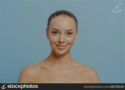 Beauty portrait of young smiling gorgeous woman with perfect clean healthy skin looking at camera isolated on blue studio background. Cosmetology, dermatology and skincare cosmtics concept. Beauty portrait of young smiling gorgeous woman with perfect clean healthy skin isolated on blue