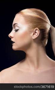 beauty portrait on black background of blonde girl in profile with white eye make-up, dark lipstick and long smooth blonde hair