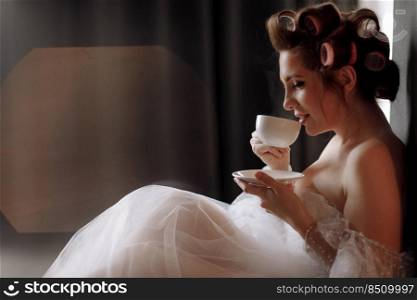 beauty portrait woman. beautiful young woman with makeup, curlerses dressed in white dress and relaxing at home holding cup of coffee or tea and looking in camera. international women’s day.. beauty portrait woman. beautiful young woman with makeup, curlerses dressed in white dress and relaxing at home holding cup of coffee or tea and looking in camera. international women’s day