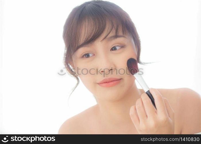 Beauty portrait young asian woman smile with face looking mirror applying makeup with brush cheek in the bedroom, beautiful of girl holding blusher, skin care and cosmetic concept.