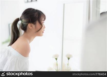 Beauty portrait young asian woman smiling look at mirror of checking skin care caucasian with wellness in the bedroom, beautiful girl happy touching face in reflection for health, lifestyle concept.