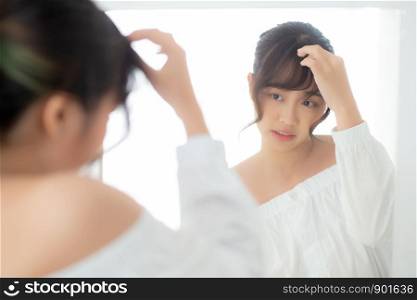 Beauty portrait young asian woman smiling look at mirror of checking skin care caucasian with wellness in the bedroom, beautiful girl happy touching face in reflection for health, lifestyle concept.
