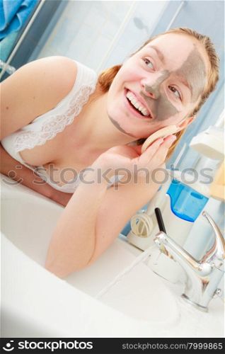 Beauty procedures spa and skin care concept. Young woman removing facial clay mud mask with sponge in bathroom