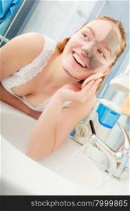 Beauty procedures spa and skin care concept. Young woman removing facial clay mud mask with sponge in bathroom