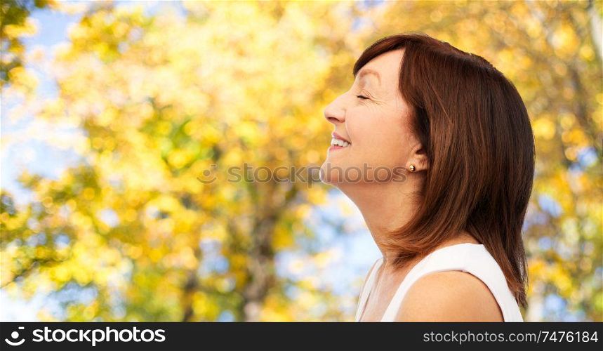 beauty, rhinoplasty and old people concept - profile of smiling senior woman over natural autumn background. profile of smiling senior woman in autumn