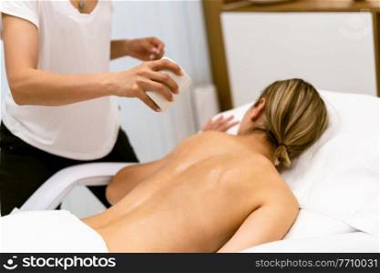Beauty salon professional pouring oil from a massage candle on the back of his female patient.. Beauty salon professional pouring oil from a massage candle on the back of his patient.