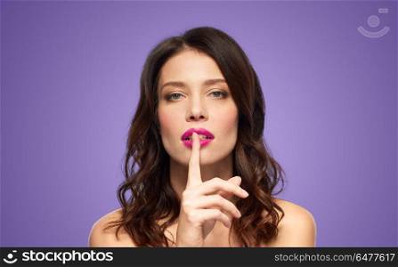 beauty, secret, make up and people concept - beautiful woman holding finger on lips or mouth with pink lipstick over ultra violet background. woman with pink lipstick holding finger on mouth. woman with pink lipstick holding finger on mouth