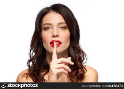 beauty, secret, make up and people concept - woman holding finger on lips or mouth with red lipstick over white background. woman with red lipstick holding finger on mouth