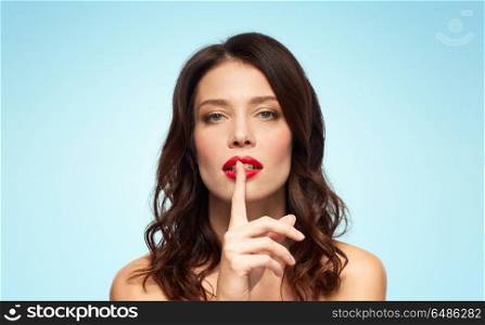 beauty, secret, make up and people concept - woman holding finger on lips or mouth with red lipstick over blue background. woman with red lipstick holding finger on mouth. woman with red lipstick holding finger on mouth