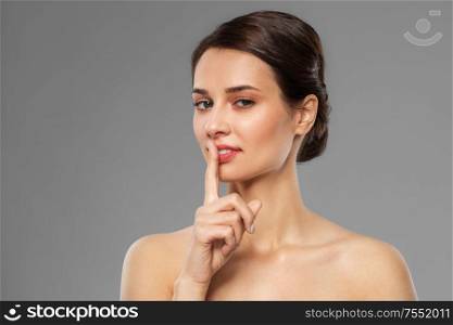 beauty secret, silence and people concept - beautiful young woman holding finger on lips over grey background. beautiful young woman holding finger on lips