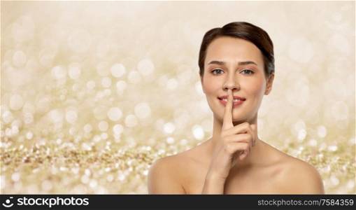 beauty secret, silence and people concept - beautiful young woman holding finger on lips over shimmering golden glitter on background. beautiful young woman holding finger on lips