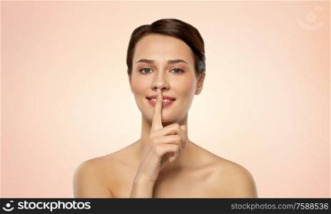 beauty secret, silence and people concept - beautiful young woman holding finger on lips over beige background. beautiful young woman holding finger on lips