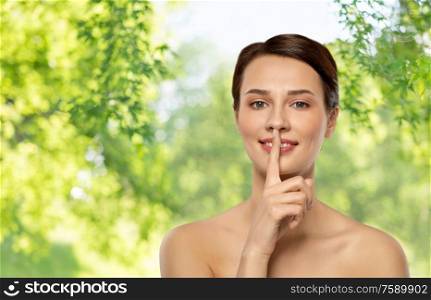 beauty secret, silence and people concept - beautiful young woman holding finger on lips over green natural background. beautiful young woman holding finger on lips