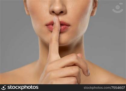 beauty secret, silence and people concept - close up of beautiful young woman holding finger on lips over grey background. beautiful young woman holding finger on lips