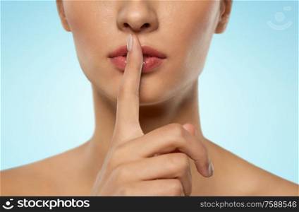 beauty secret, silence and people concept - close up of beautiful young woman holding finger on lips over blue background. beautiful young woman holding finger on lips
