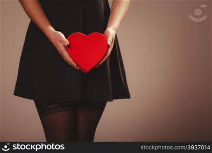 Beauty, sexuality and seductiveness. Sexy part body woman wearing black dress and stockings panties holding red heart box present gift in hands. Studio shot.