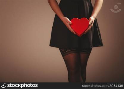 Beauty, sexuality and seductiveness. Sexy part body woman wearing black dress and stockings panties holding red heart box present gift in hands. Studio shot.