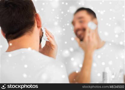 beauty, shaving, grooming and people concept - close up of man applying shaving foam to face and looking to mirror at home bathroom over snow