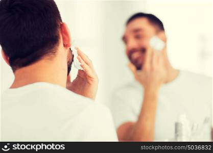 beauty, shaving, grooming and people concept - close up of man applying shaving foam to face and looking to mirror at home bathroom. close up of man applying shaving foam to face