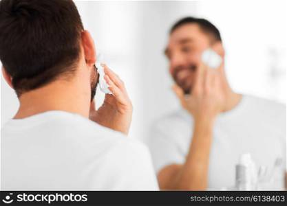 beauty, shaving, grooming and people concept - close up of man applying shaving foam to face and looking to mirror at home bathroom