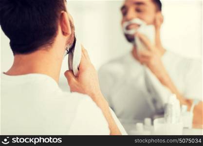 beauty, shaving, grooming and people concept - close up of man removing shaving foam from face with towel and looking to mirror at home bathroom. close up of man removing shaving foam from face