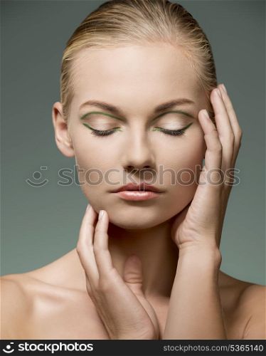 beauty shoot of sexy blonde woman with calm expression, naked shoulders, perfect visage skin and creative green make-up posing with hands near her face