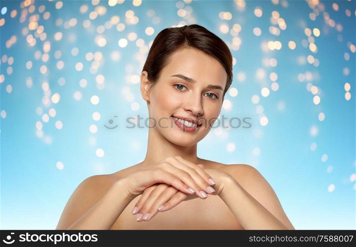 beauty, skin care and bodycare concept - beautiful young woman moisturizing her hands over holidays lights on blue background. beautiful young woman moisturizing her hands skin