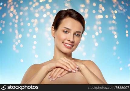 beauty, skin care and bodycare concept - beautiful young woman moisturizing her hands over holidays lights on blue background. beautiful young woman moisturizing her hands skin