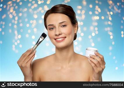 beauty, skin care and cosmetics concept - beautiful young woman with facial mask and brush over holidays lights on blue background. beautiful young woman with facial mask and brush
