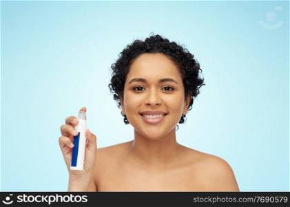 beauty, skin care and cosmetics concept - portrait of happy smiling young african american woman with bare shoulders with spray bottle over blue background. happy african woman with spray bottle