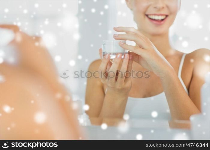 beauty, skin care and people concept - close up of smiling young woman with face cream mirror reflection at home bathroom over snow