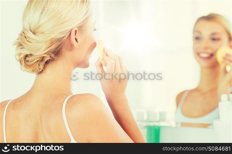 beauty, skin care and people concept - close up of smiling young woman washing her face with facial cleansing sponge at home bathroom. close up of woman washing face with sponge at home. close up of woman washing face with sponge at home