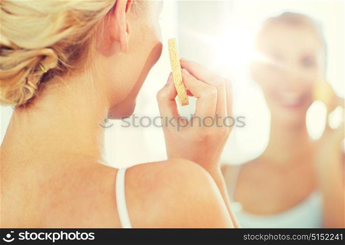 beauty, skin care and people concept - close up of smiling young woman washing her face with facial cleansing sponge at home bathroom. close up of woman washing face with sponge at home