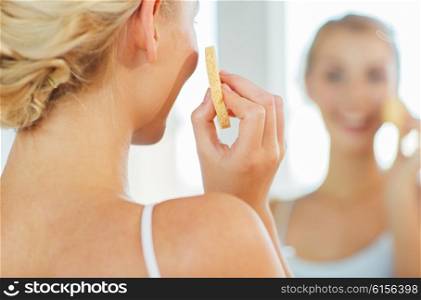 beauty, skin care and people concept - close up of smiling young woman washing her face with facial cleansing sponge at home bathroom