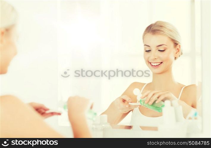 beauty, skin care and people concept - smiling young woman applying lotion to cotton disc for washing her face at bathroom. young woman with lotion washing face at bathroom. young woman with lotion washing face at bathroom